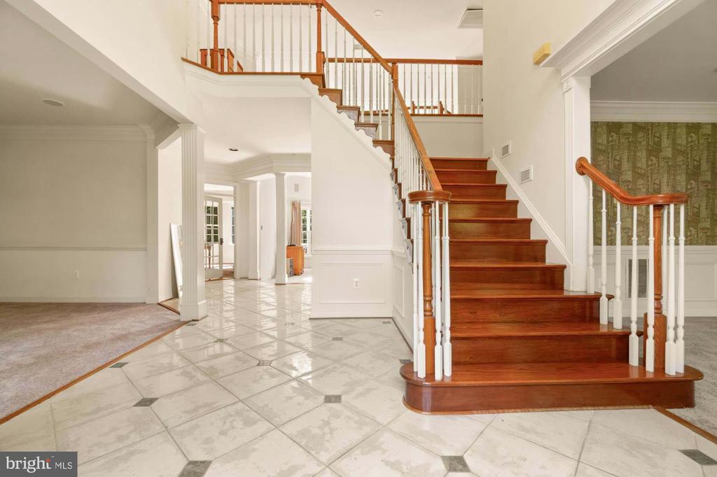 Foyer with marble-tile flooring and a curved wooden staircase with white balusters.