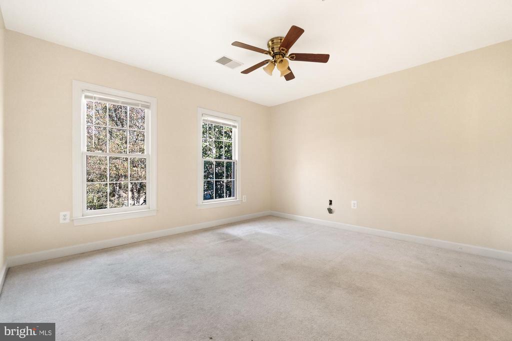 Empty bedroom with two windows, beige walls, light carpet, and a ceiling fan.