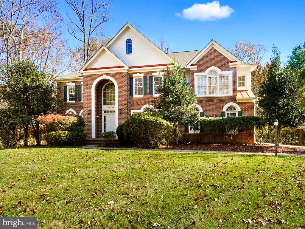 Two-story brick house with white gables, an arched entry, and shrubs along the front lawn.