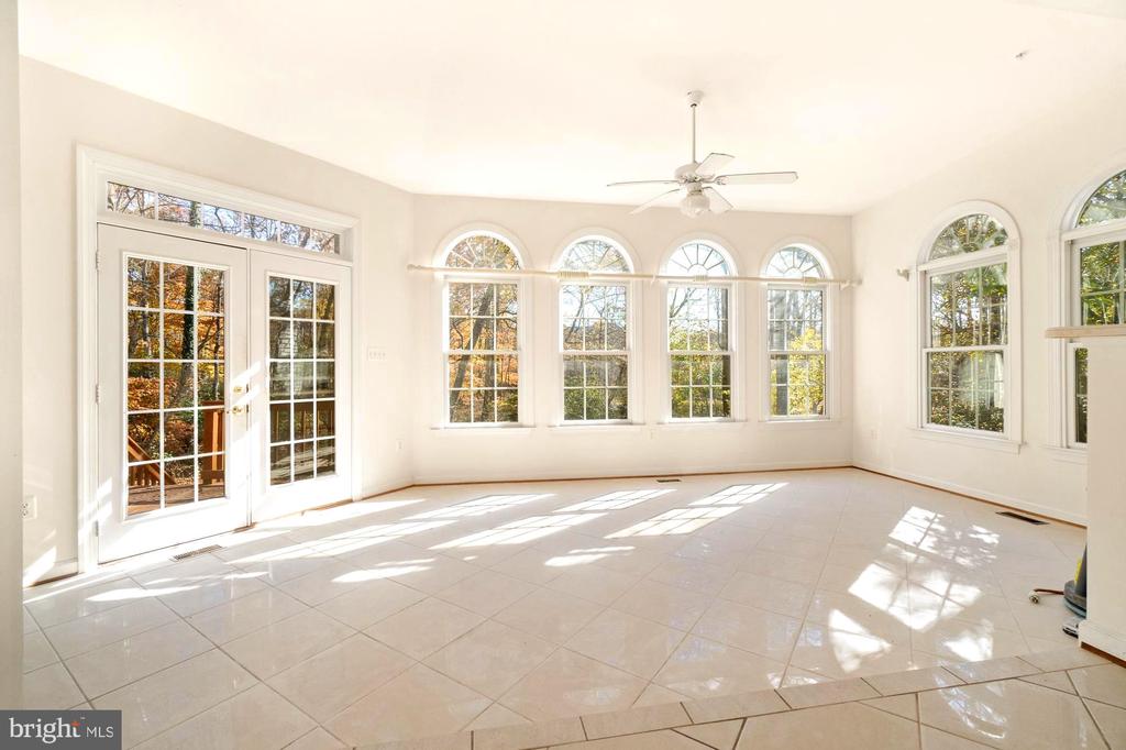 Vacant sunroom with tiled floors, French doors, and arched windows overlooking trees.