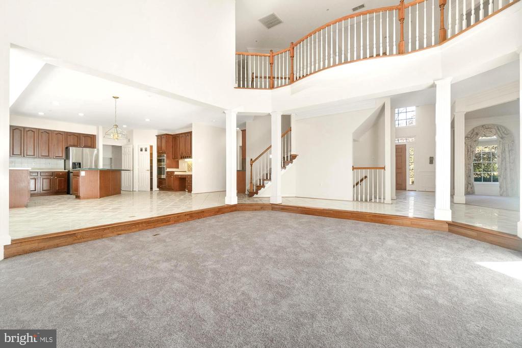 Open living room with gray carpet, raised tiled kitchen, and upstairs balcony railing.