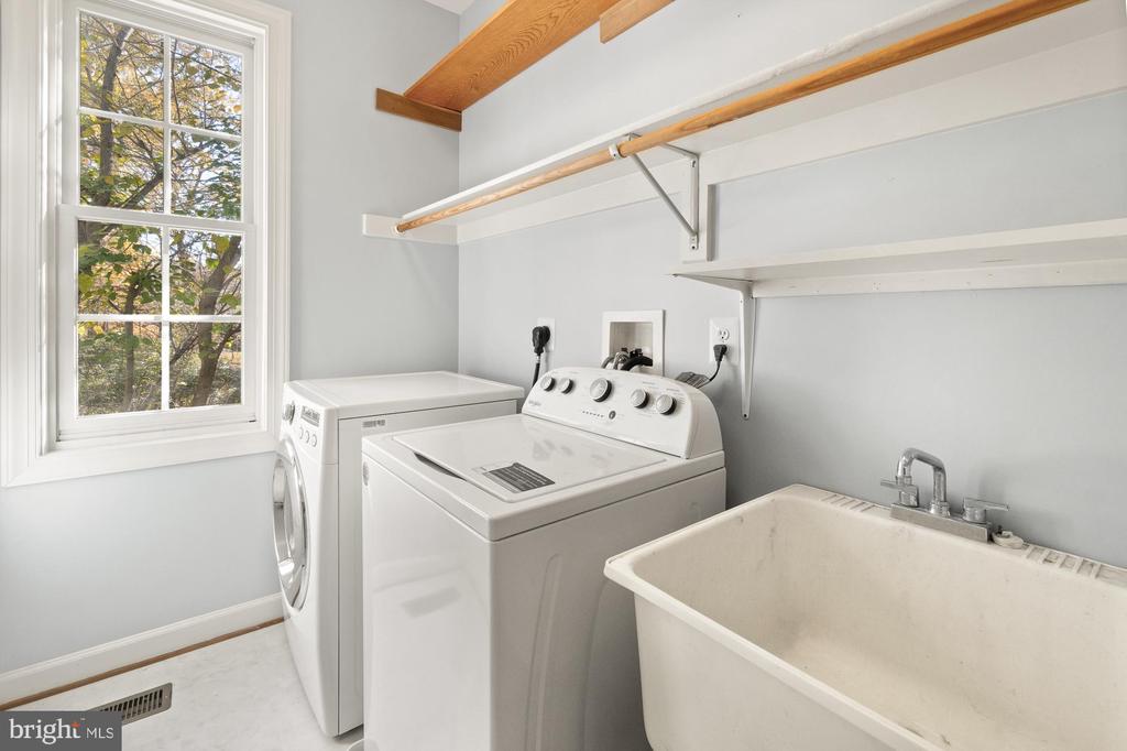 Laundry room with washer and dryer, deep utility sink, and window overlooking trees.