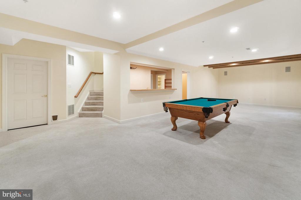 Basement recreation room with a pool table, carpeted floor, stairway, and serving pass-through.