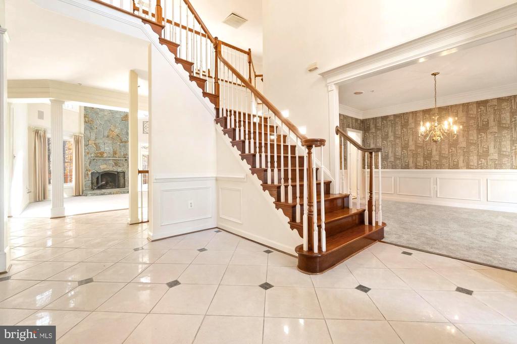 Foyer with a sweeping wooden staircase, glossy tile floors, and adjoining dining room.