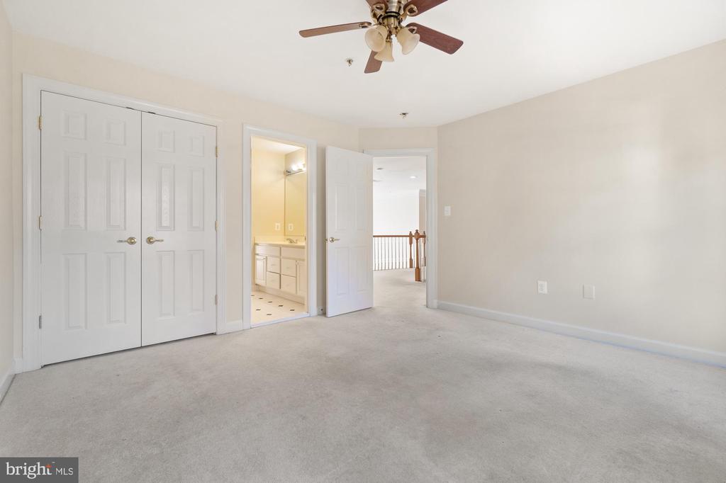 Empty carpeted bedroom with a ceiling fan, double closets, and an adjoining bathroom.