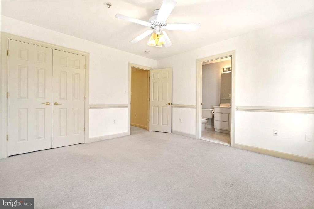 Empty carpeted bedroom with double closets, a ceiling fan, and an adjoining bathroom.