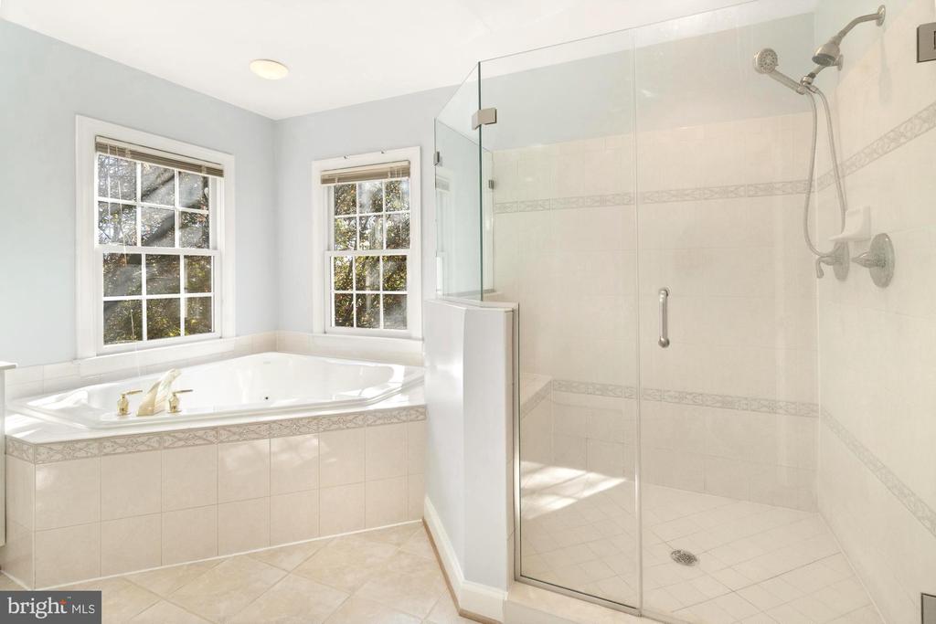 Bathroom with a corner soaking tub, two windows, and a glass-enclosed tiled shower.