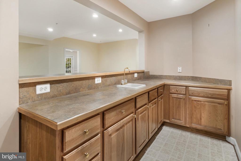 Bathroom vanity with a long countertop, single sink, large mirror, and wood cabinetry.