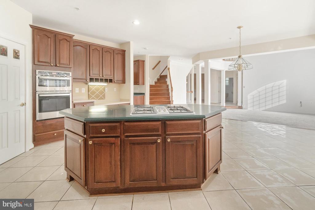 Kitchen with a large cooktop island, dark wood cabinetry, and built-in wall ovens.