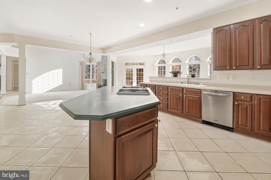 Kitchen with a large cooktop island, dark wood cabinetry, stainless dishwasher, and arched windows.