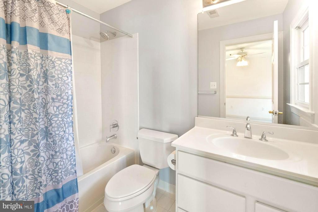 Bathroom with a white tub, patterned blue shower curtain, toilet, and vanity beside a window.
