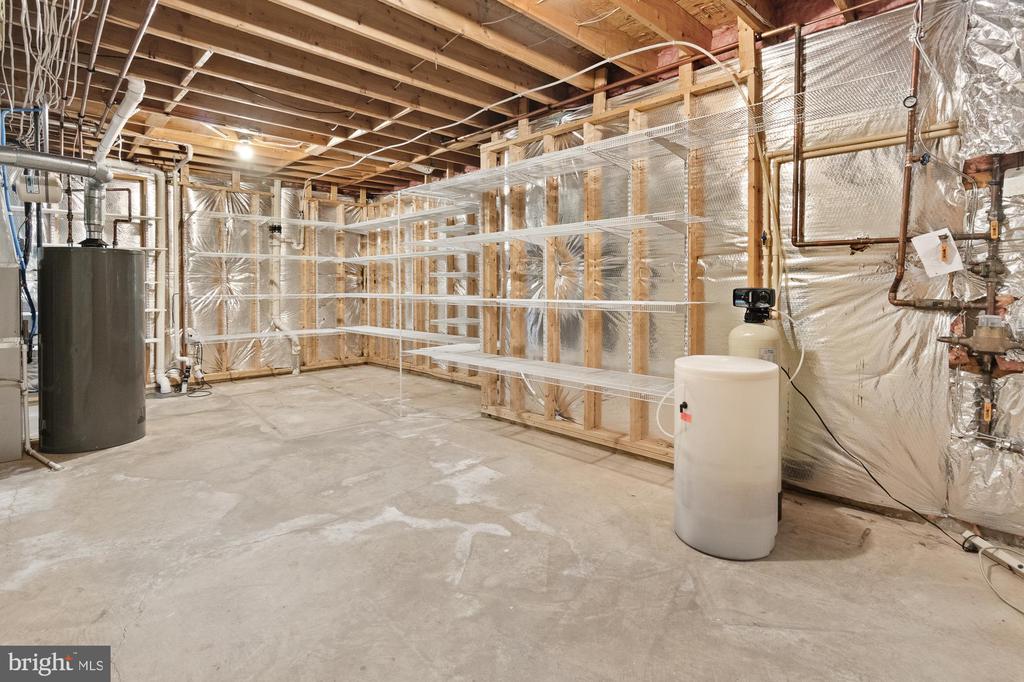 Unfinished basement with exposed framing, utility tanks, and wire shelving.
