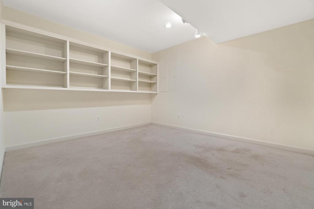 Vacant carpeted room with long built-in white shelving and recessed ceiling lights.