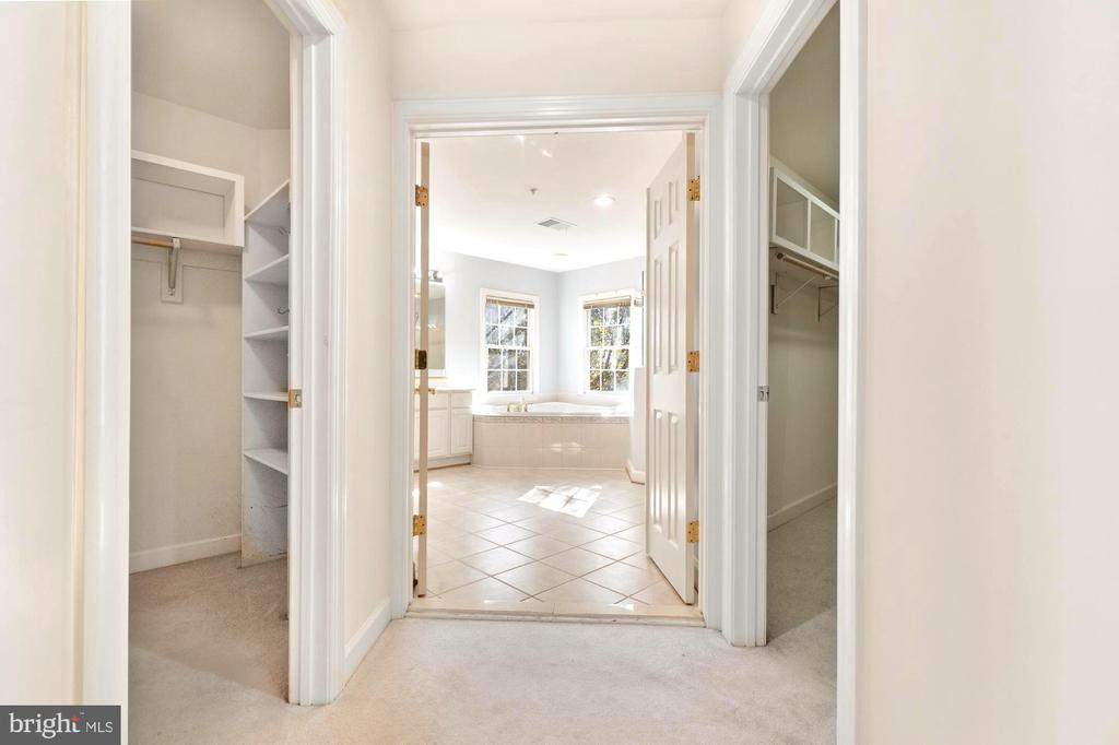Bathroom with a soaking tub beneath two windows, viewed through open closets.