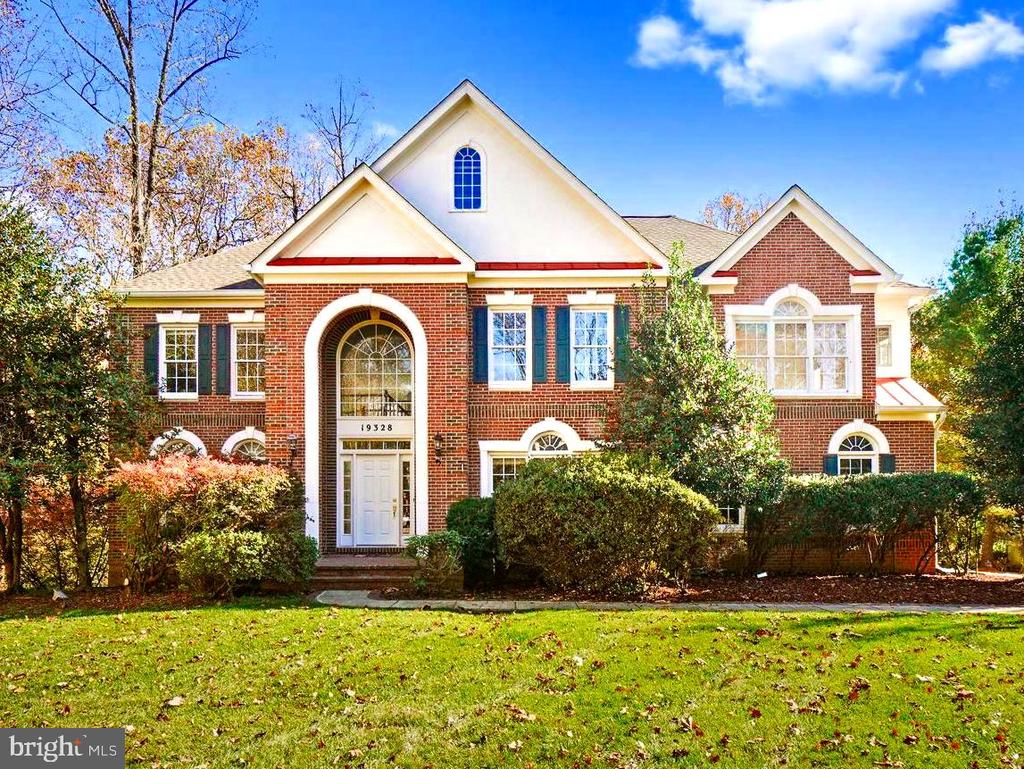 Red-brick home with white gables, an arched front entrance, blue shutters, and a green lawn.