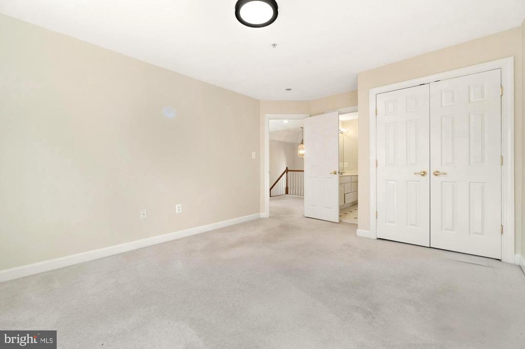 Empty carpeted bedroom with double closet doors and an open doorway to the bathroom.
