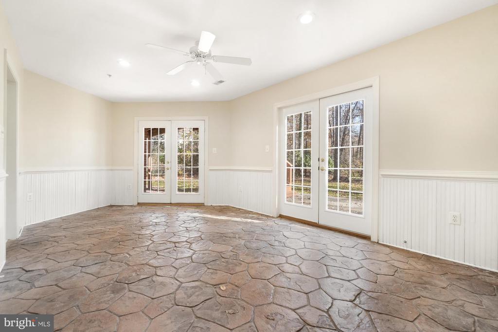 Empty room with an irregular stone floor, white wainscoting, and French doors to the yard.
