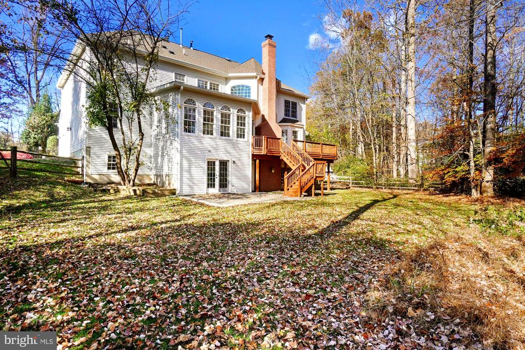 Rear of a white two-story house with a raised deck and leaf-covered yard.