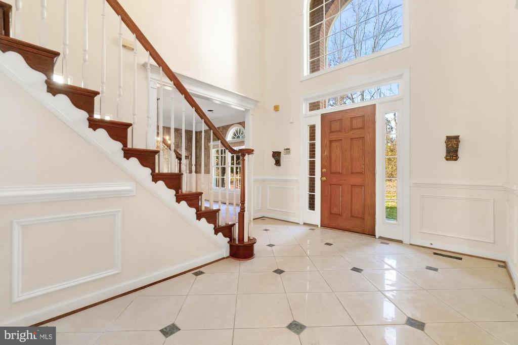 Two-story foyer with a sweeping wood-railed staircase, tiled floor, and front door beneath an arched window.