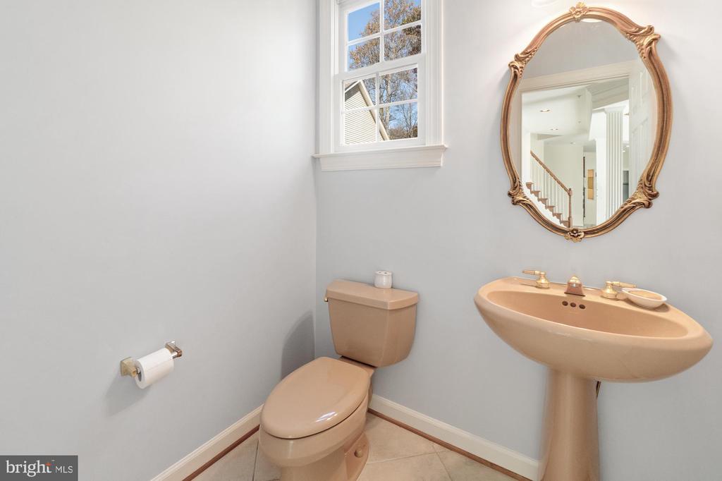 Bathroom with a beige pedestal sink, ornate mirror, and window above the toilet.