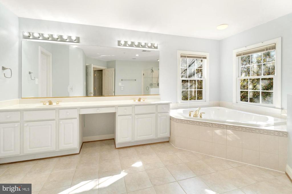 Bathroom with a long white vanity, large mirror, and corner soaking tub beneath two windows.