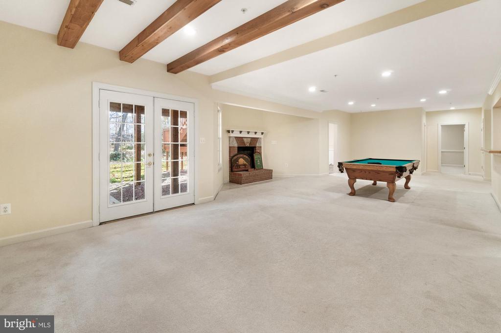 Carpeted recreation room with exposed beams, a brick fireplace, French doors, and a pool table.