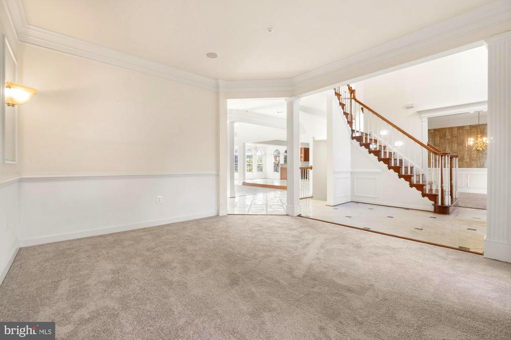 Carpeted room opening to a tiled foyer with a wooden staircase and white balusters.