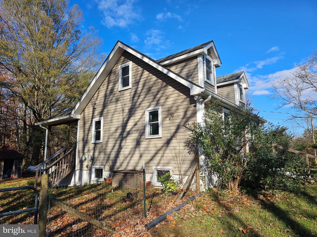 Tan-sided house with white trim, roof dormers, covered porch, and fenced yard.