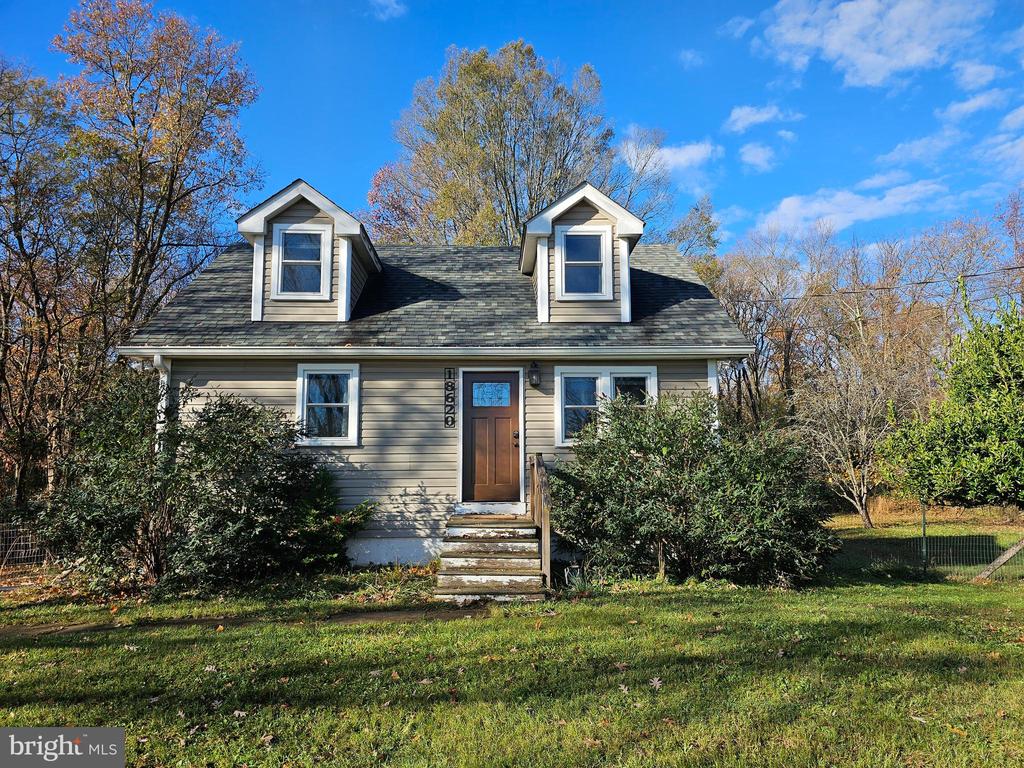 Gray-sided house with two dormer windows, front steps, and shrubs along the entrance.