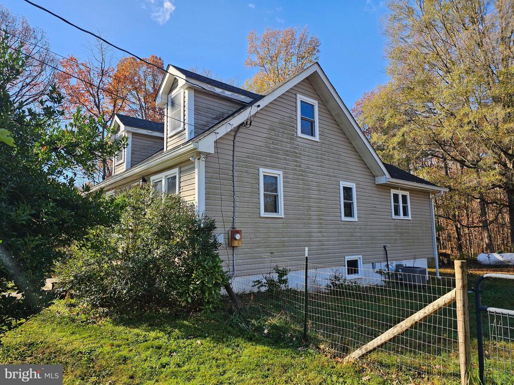 Gray-sided house with white trim and dormers behind a fenced yard and autumn trees.