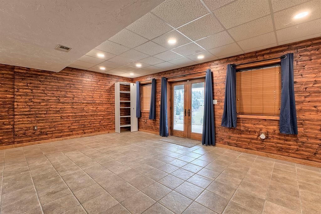 Empty room with rustic wood walls, tiled floor, and glass double doors with dark curtains.