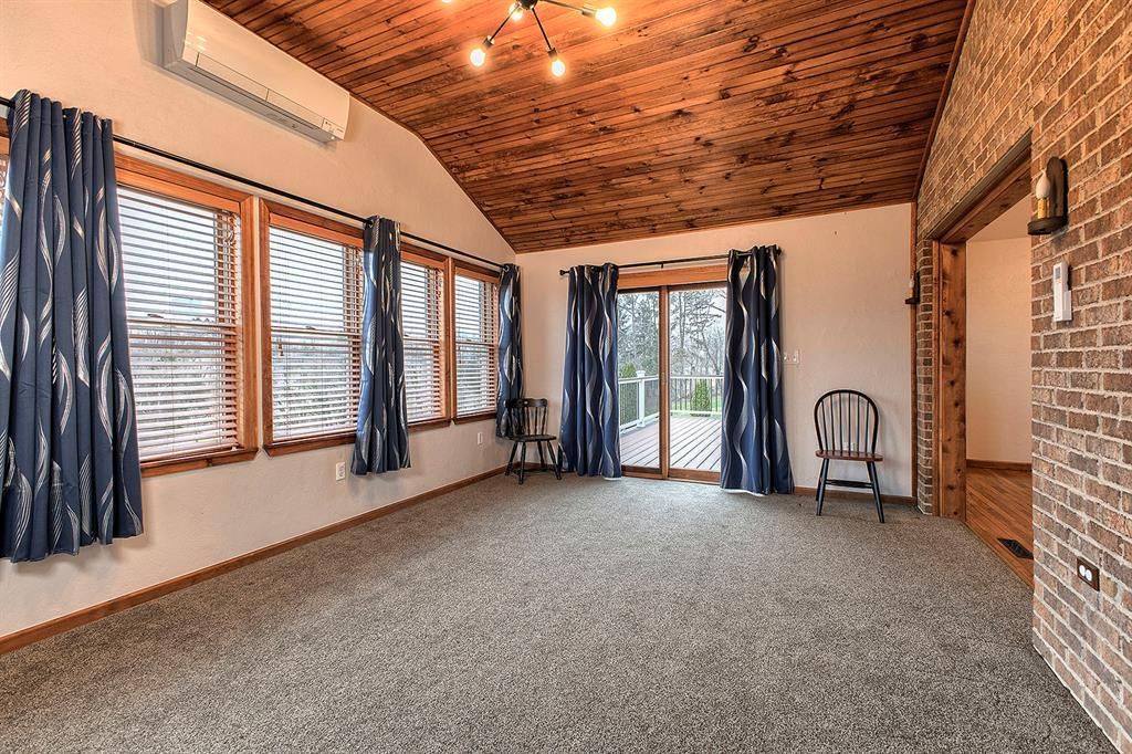 Living room with a vaulted wood ceiling, brick wall, and sliding doors to a deck.