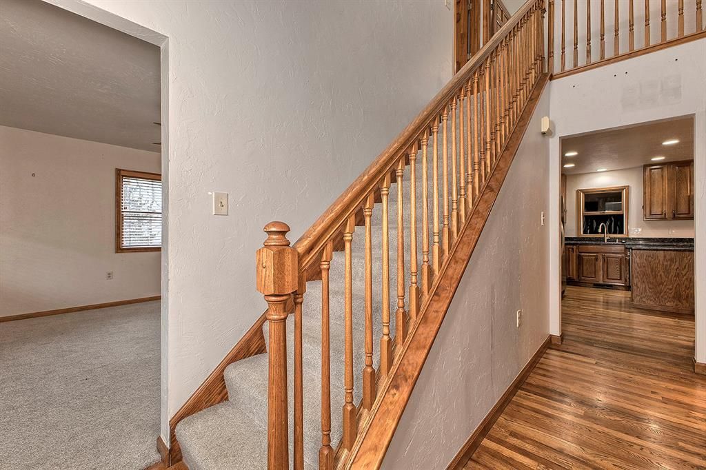 Wooden staircase with carpeted steps beside a hardwood-floored entry and a glimpse of the kitchen.