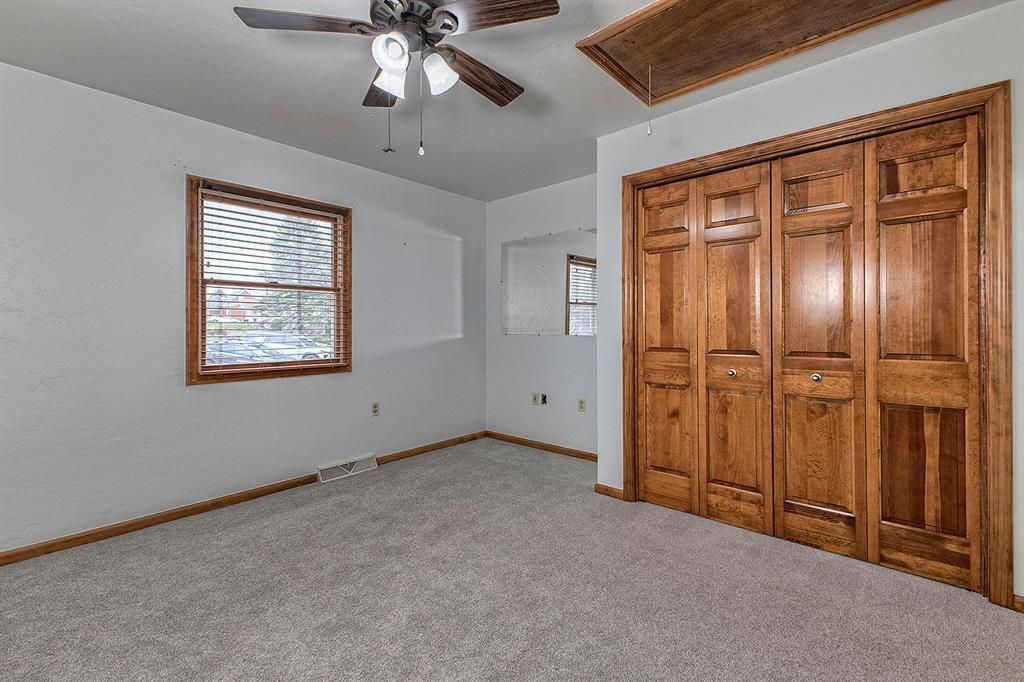 Empty bedroom with gray carpet, wooden closet doors, and a window with blinds.