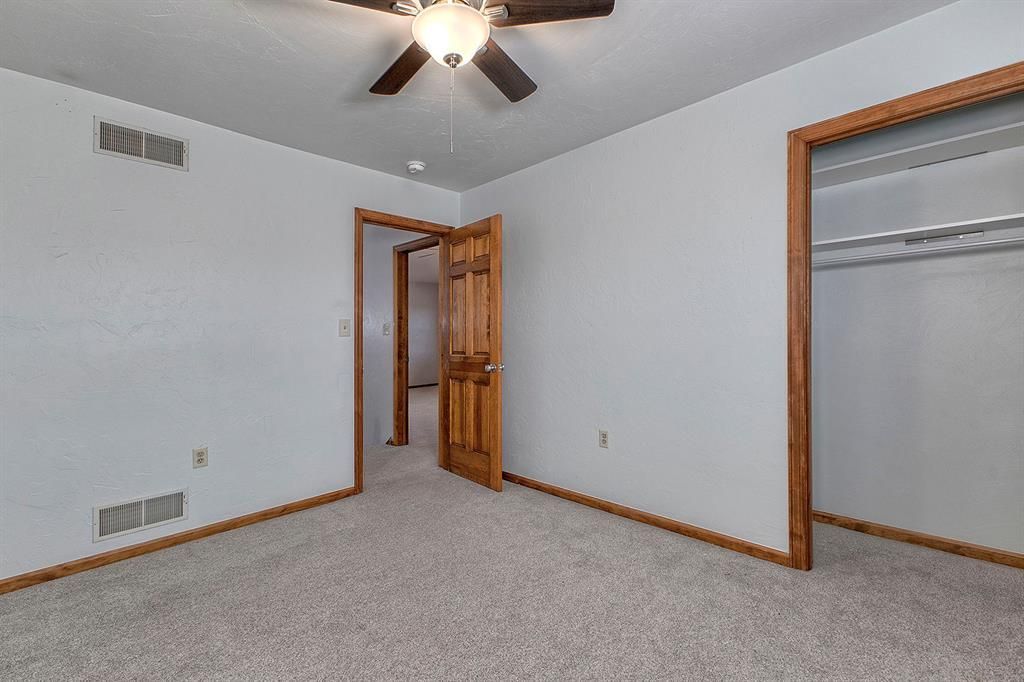 Empty bedroom with gray carpet, wood trim, and a ceiling fan.
