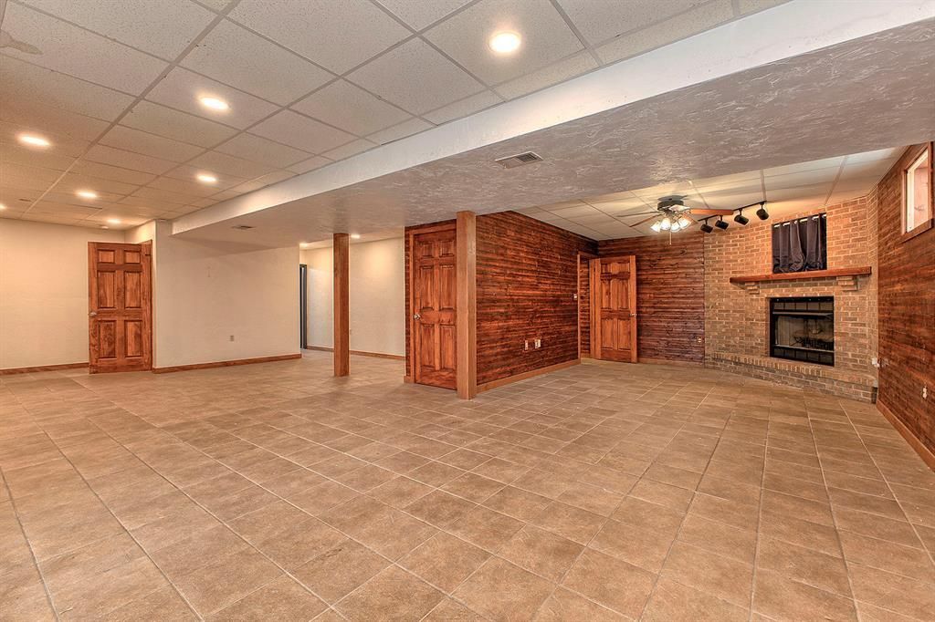 Vacant basement recreation room with tiled floors, dark wood paneling, and a brick fireplace.