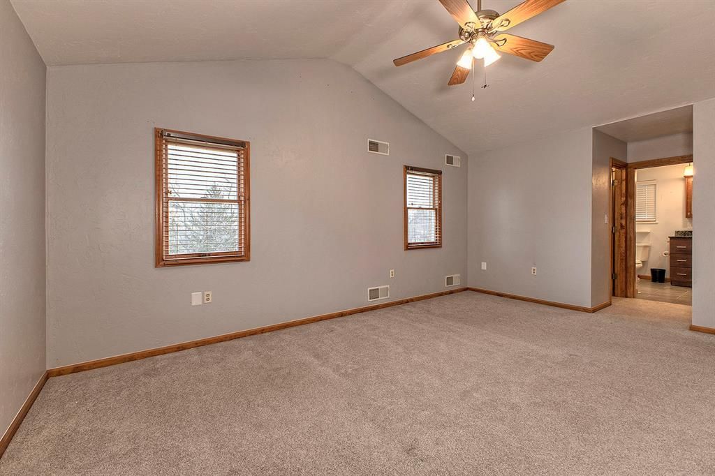 Empty carpeted room with two windows, a vaulted ceiling, and a ceiling fan.