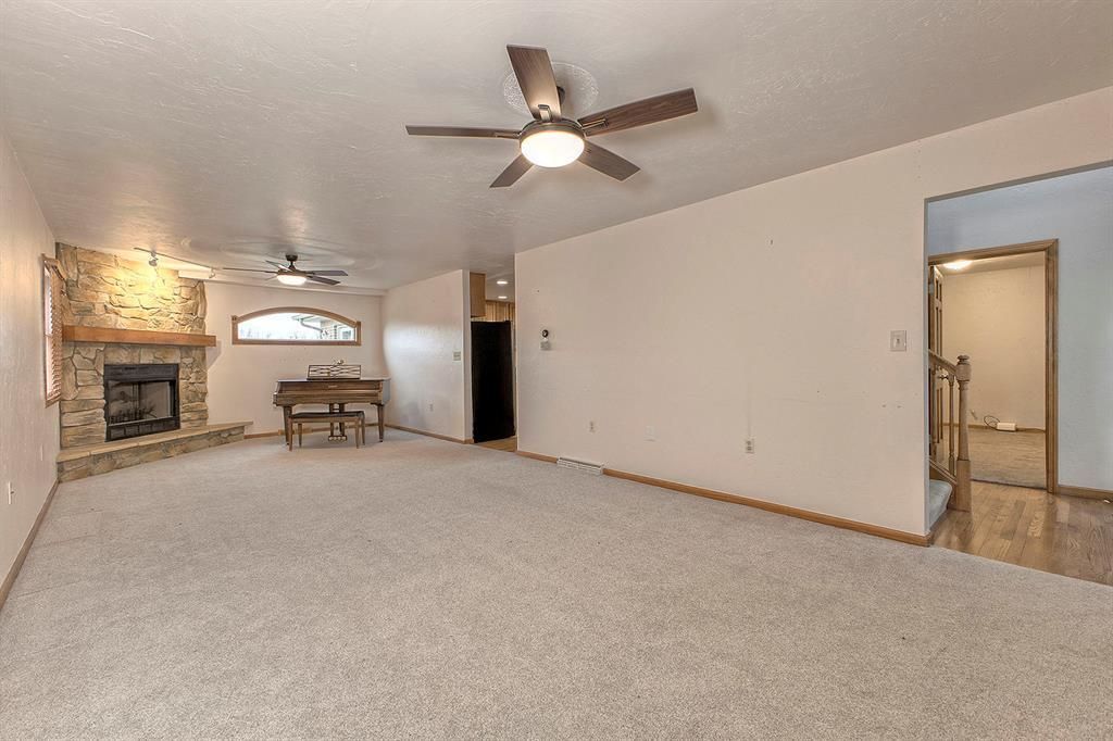 Carpeted living room with a stone fireplace, piano, and two ceiling fans.
