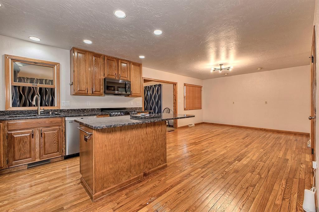 Open-plan kitchen with a wood island, granite counters, and hardwood floors adjoining an unfurnished dining area.