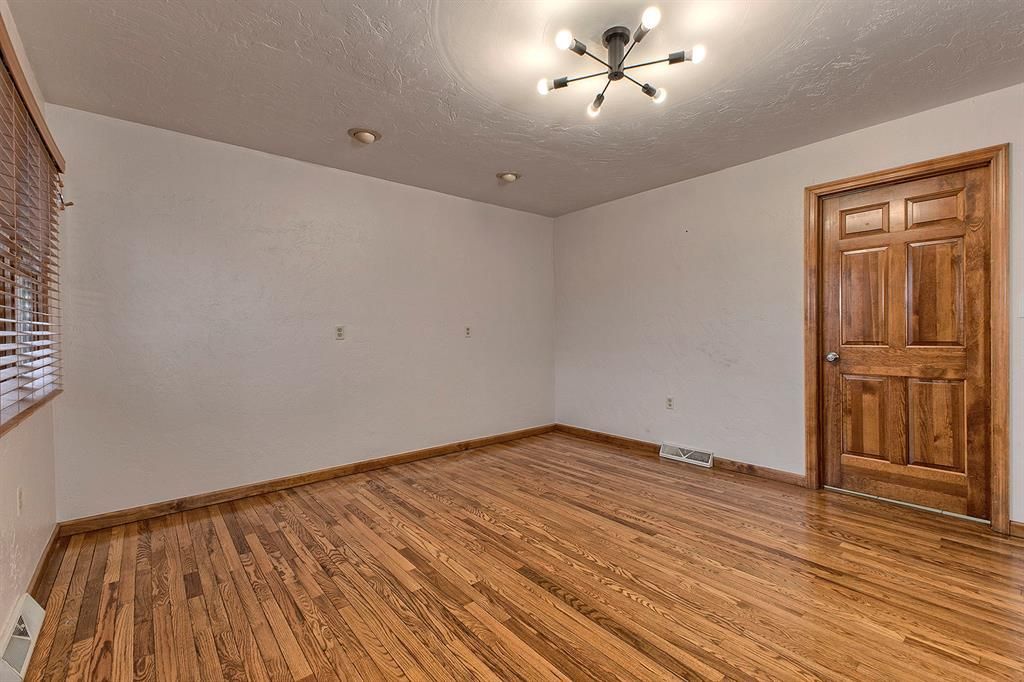 Empty room with hardwood floors, a modern ceiling light, and a wooden paneled door.