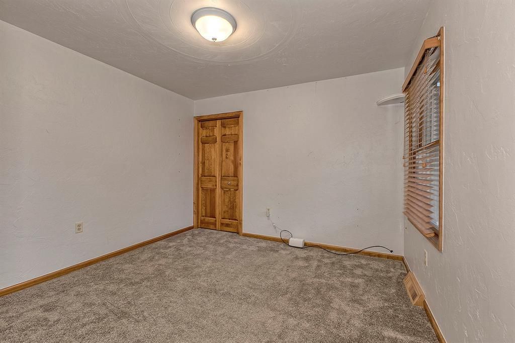 Empty carpeted room with a wooden paneled door and a window with wooden blinds.