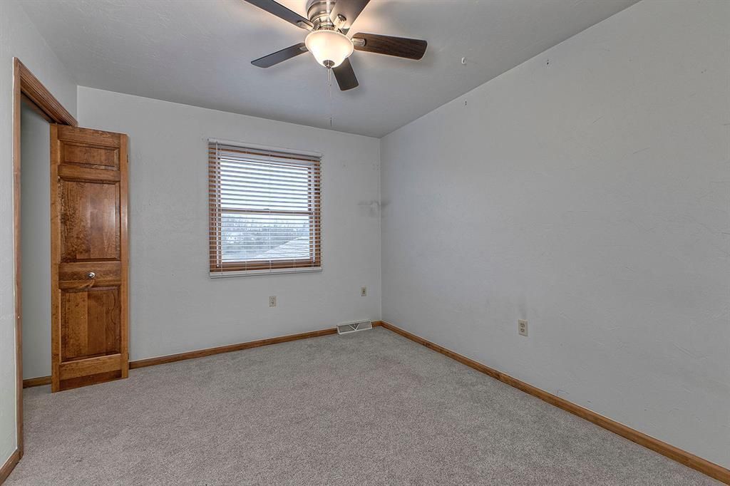 Empty bedroom with a ceiling fan, gray carpet, and wood-trimmed window with blinds.