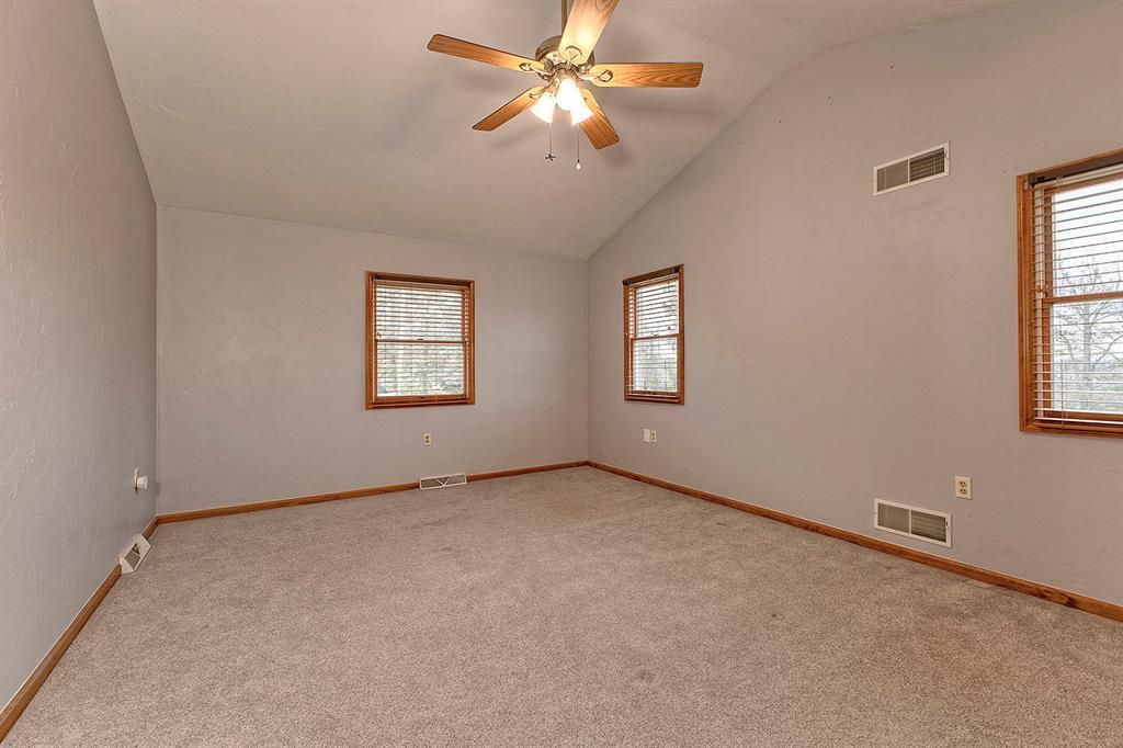 Empty bedroom with beige carpet, three windows with wooden blinds, and a ceiling fan.