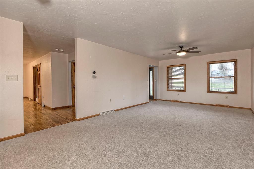 Empty living room with beige carpet, two wood-trimmed windows, and a ceiling fan.
