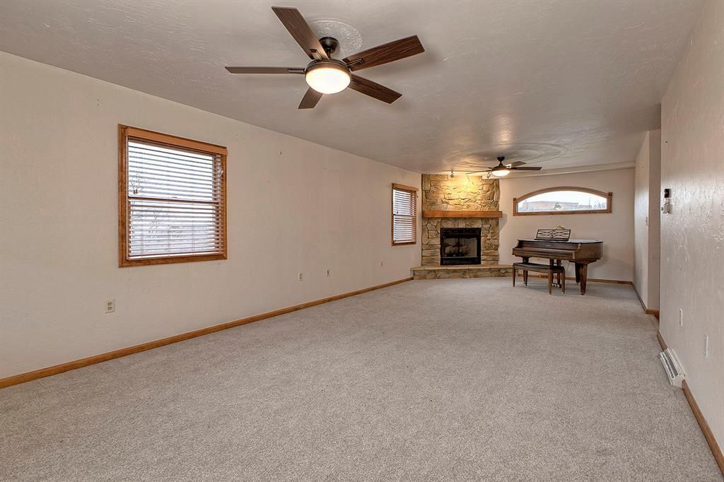 Living room with a stone fireplace, piano, beige carpet, and ceiling fans.