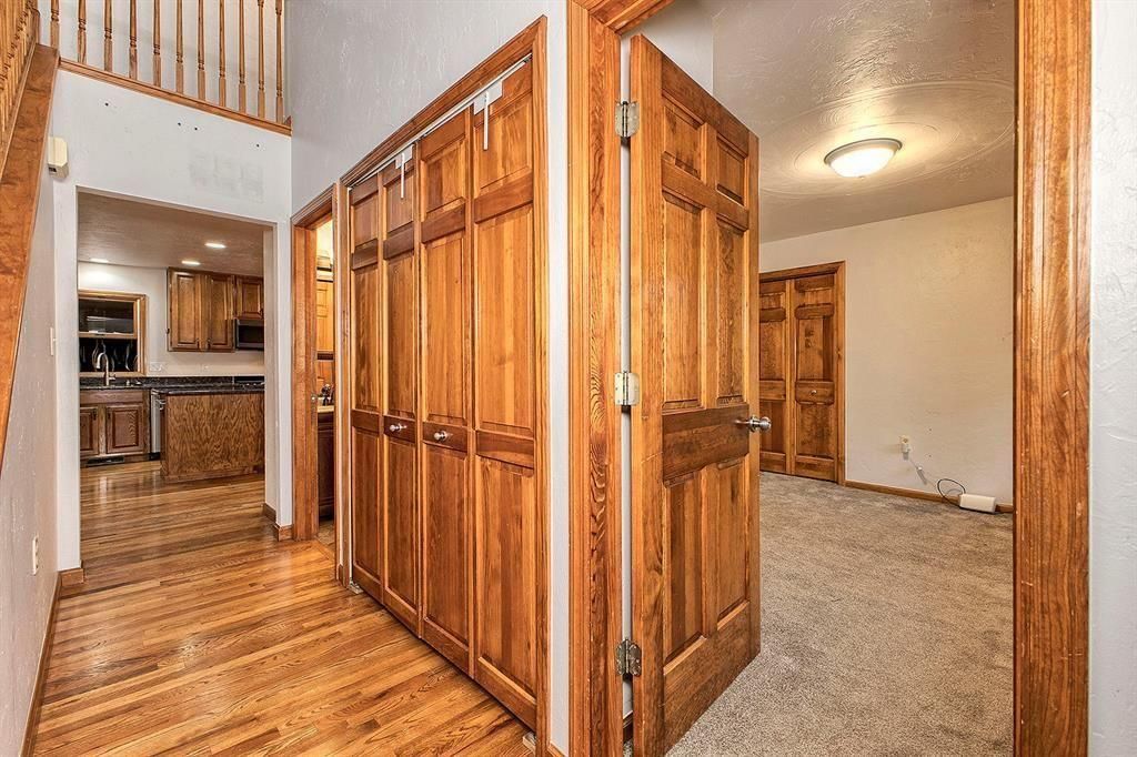 Hallway with hardwood floors and wood-paneled closets between the kitchen and a carpeted room.