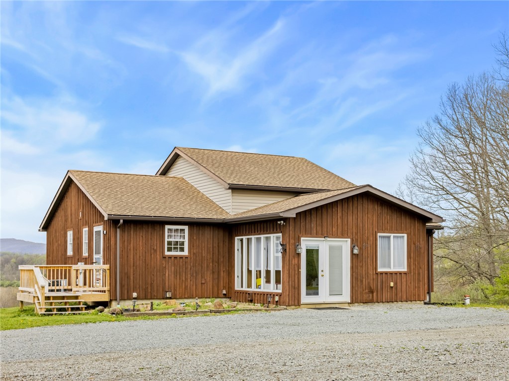 Brown wood-sided house with a small deck and gravel driveway.