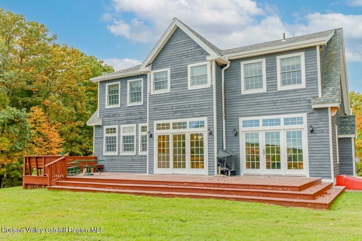 Gray two-story house with a broad redwood deck and autumn trees.