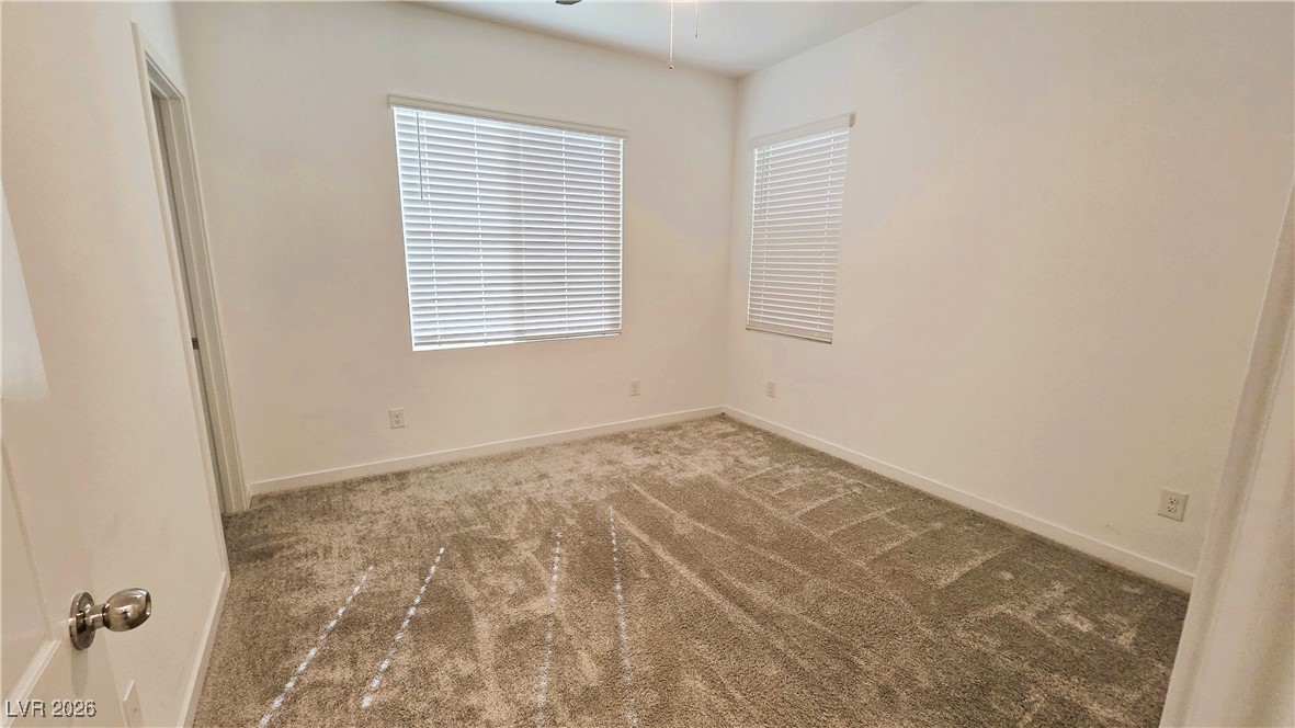 Empty carpeted bedroom with two windows fitted with white blinds.