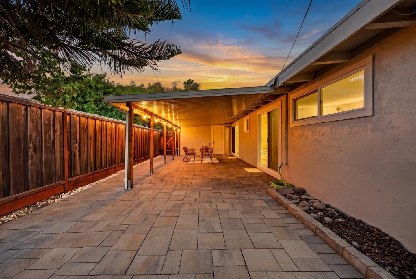 Paved backyard patio with a covered seating area and string lights at dusk.